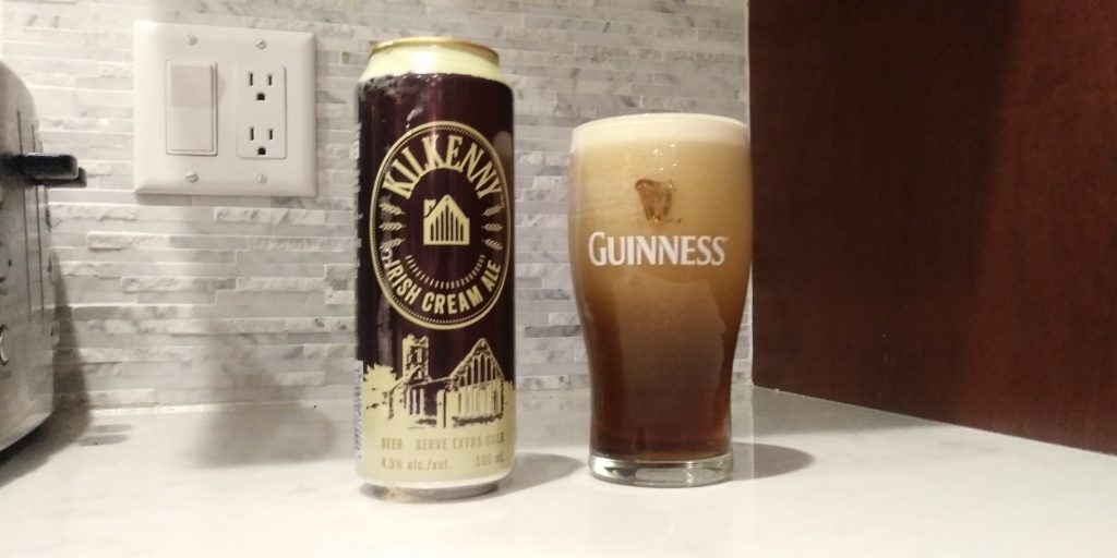 Foam drips down an empty can of Kilkenny nitro brew cream ale as nitrogen bubbles cascade through a freshly poured glass turning from pale cream at the head to tan beer at the base.